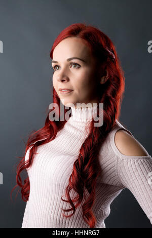 Portrait de jeune femme aux longs cheveux rouges, fond gris Banque D'Images