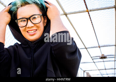 Portrait of smiling Asian woman wearing hoodie androgyne Banque D'Images