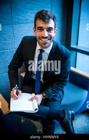 Smiling Hispanic businessman writing on notepad in office lounge Banque D'Images