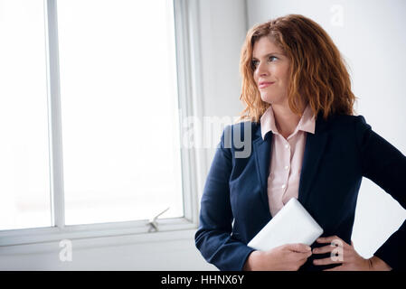 Smiling Caucasian businesswoman holding digital tablet fenêtre proche Banque D'Images