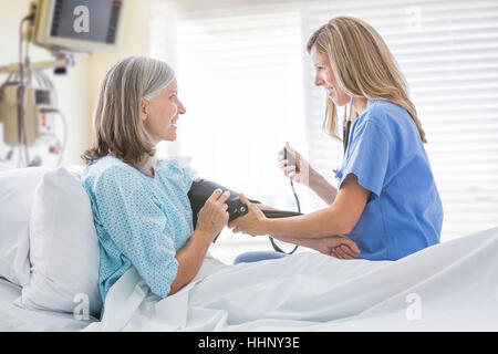 Caucasian nurse la mesure de la pression artérielle de woman in hospital bed Banque D'Images