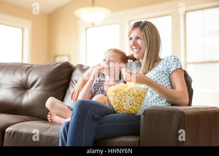 Caucasian mother and daughter sitting on sofa eating bol de maïs soufflé Banque D'Images