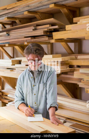 Caucasian carpenter écrit sur le bloc-notes en atelier Banque D'Images