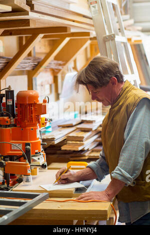 Caucasian carpenter écrit sur le bloc-notes en atelier Banque D'Images