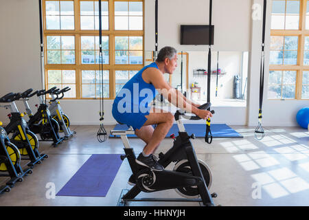 Mixed Race man riding stationary bicycle in gymnasium Banque D'Images