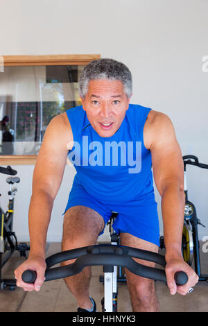 Mixed Race man riding stationary bicycle in gymnasium Banque D'Images