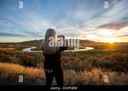 Caucasian woman photographing coucher de soleil sur la rivière sinueuse Banque D'Images