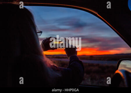 Caucasian woman in car photographier le coucher du soleil avec cell phone Banque D'Images