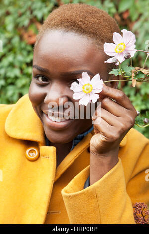 Portrait of smiling black woman couvrant de fleurs avec des yeux Banque D'Images