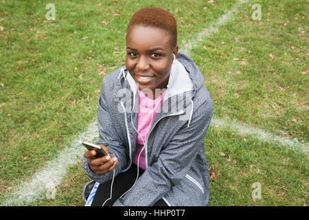 Black woman sitting on écoute de champ cell phone Banque D'Images