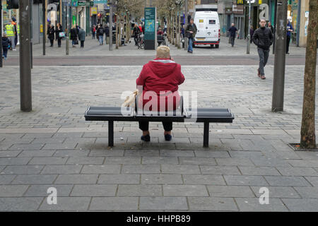 Vieille Grande dame sur téléphone mobile en rouge assis sur le banc de la rue Sauchiehall Street, Glasgow Banque D'Images