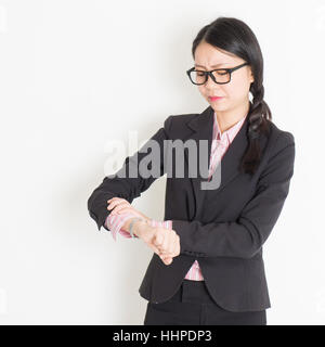 Young Asian businesswoman vérifie de temps à sa montre-bracelet, fin concept, debout sur fond uni. Banque D'Images