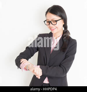 Young Asian businesswoman vérifie de temps à sa montre-bracelet, debout sur fond uni. Banque D'Images