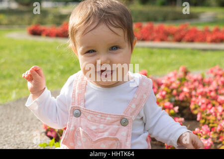 Petite fille en rose est assis sur le pré vert et jouer avec des fleurs Banque D'Images