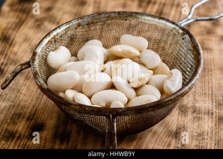Tamis ou passoire avec des haricots blancs sur une planche de bois. Banque D'Images