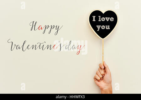 Happy Valentines Day le texte écrit sur un fond blanc et une pancarte en forme de coeur avec le texte je t'aime écrit en C dans la main d'un Banque D'Images