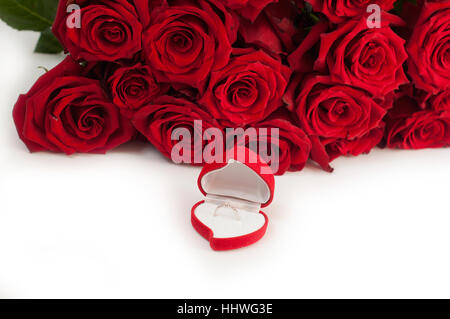 Bague de fiançailles en or blanc avec diamants dans une boîte en forme de coeur et roses sur fond isolé blanc Banque D'Images