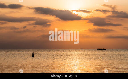 Coucher de soleil sur la mer, pêcheur debout dans l'eau, rétro-éclairé, plage de Lovina, Bali, Indonésie Banque D'Images