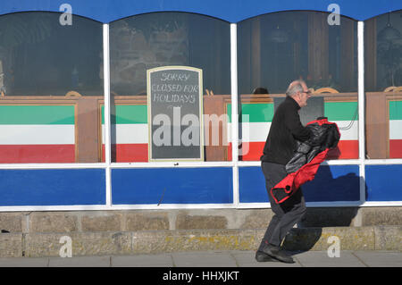 Un homme pressé en passant devant un café fermé pour l'hiver dans la région de Cornwall. Banque D'Images