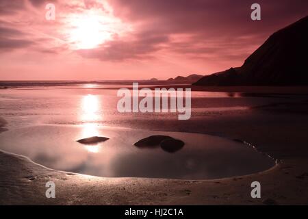 Le soleil sur le point d'établir dans un ciel rose sur la plage dans l'ouest du pays de Galles Newgale, UK Banque D'Images