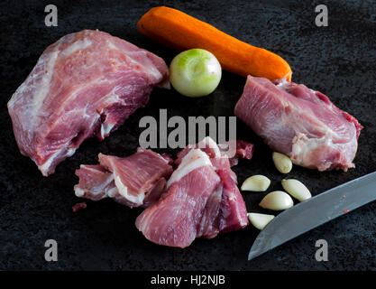 Commune de matières premières de viande de porc, oignon, ail et carotte au fond de la pierre sombre Banque D'Images