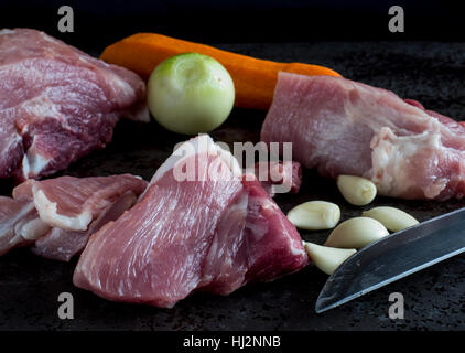 Commune de matières premières de viande de porc, oignon, ail et carotte au fond de la pierre sombre Banque D'Images