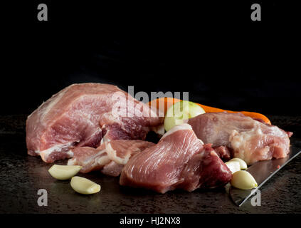 Commune de matières premières de viande de porc, oignon, ail et carotte au fond de la pierre sombre Banque D'Images