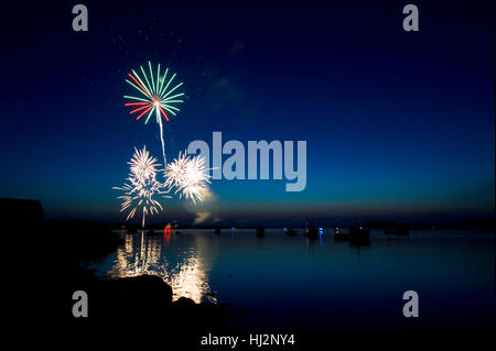 D'artifice de couleurs explosent dans un port du Maine au crépuscule rempli de bateaux. Banque D'Images