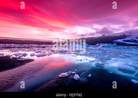 Les icebergs Jokulsarlon glacial lagoon lors d'un coucher de soleil rouge vibrant repose immobile comme il est entouré par l'eau de mer froide. Banque D'Images