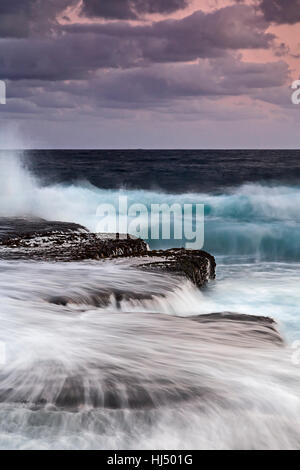 De soleil colorés sur le surf océan ouvert à partir de la plage d'eau douce côte quand nouvelle vagues splash en rochers escarpés de la côte du Pacifique de l'Australie. Banque D'Images