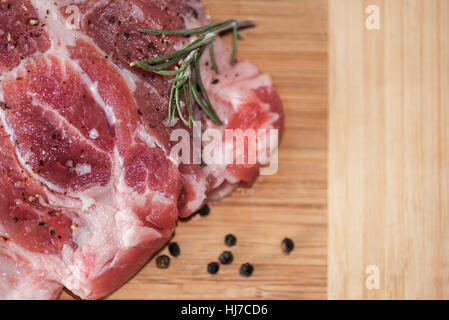 Steak de porc cru sur planche de bois. Banque D'Images