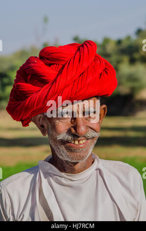 Closeup portrait of a Senior citizen Rajasthani dans sa ferme wearing red turban traditionnel Banque D'Images