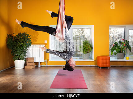 Young woman doing yoga anti-gravité au studio de bien-être avec des murs jaunes Banque D'Images