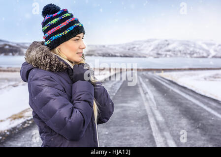 Portrait d'une jolie femme sur la route d'hiver, porter un manteau et chapeau élégant, profitant de conditions météorologiques extrêmes, Scandinave froid vacances d'hiver, l'Islande Banque D'Images