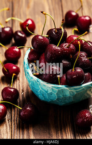 Les cerises dans un bol avec de l'eau gouttes close up sur fond de bois Banque D'Images