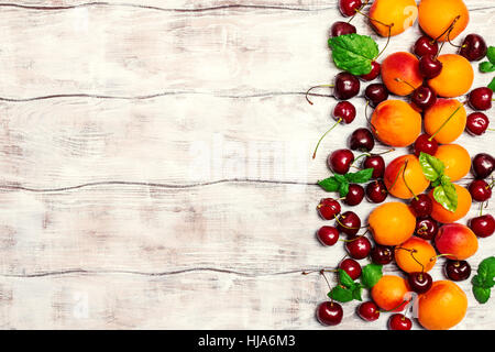 Les fruits d'été sur table en bois blanc. Les abricots et les cerises sur fond rustique, vue du dessus, copy space Banque D'Images