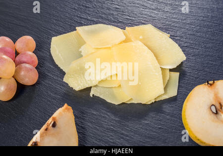 Vue de dessus de fine tranche jaune frais savoureux fromage parm, essence de poire et raisin noir sur fond ardoise, Close up Banque D'Images