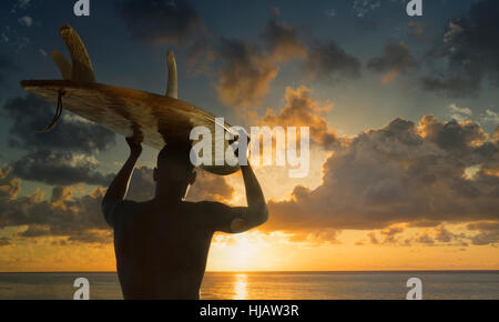Vue arrière de la silhouette homme surfer carrying surfboard on head regardant le coucher du soleil sur la mer, Rio de Janeiro, Brésil Banque D'Images