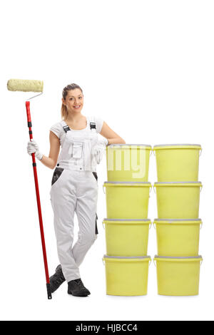 Portrait d'une femme peintre tenant un rouleau à peindre et s'appuyant sur une pile de seaux de couleur isolé sur fond blanc Banque D'Images