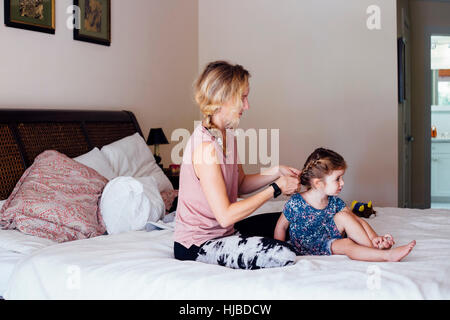 Femme assise sur le lit enfant à tresser les cheveux de sa fille Banque D'Images