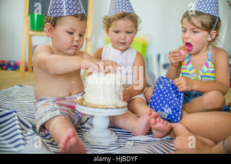 Frères et sœurs à fouiner au garçon les doigts dans le gâteau d'anniversaire Banque D'Images