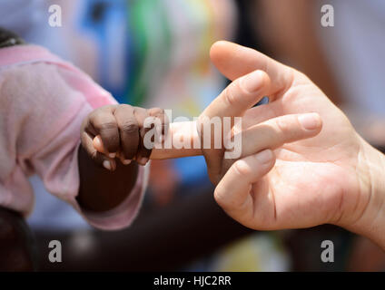 Bébé noir et blanc femme détient les mains avec un petit bébé fille africaine indigène, à Bamako, Mali. Symbole de la paix sur terre. Un beau coup avec beaucoup de p Banque D'Images