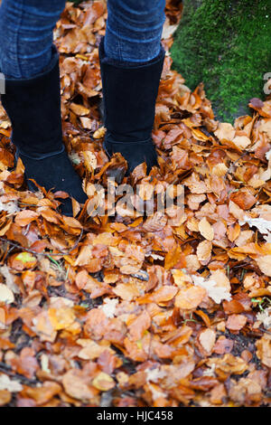 Gros plan d'une des filles pieds porter des bottes, debout dans un tapis de feuilles tombées Banque D'Images