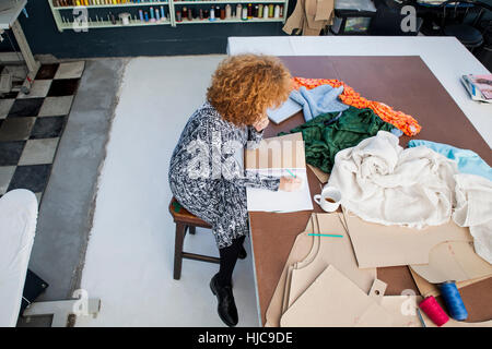 High angle view of mature female fashion designer dessin dans sketchbook à table d'atelier Banque D'Images