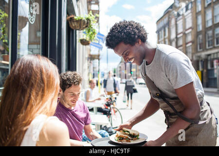 Waiter serving lunch au couple at city sidewalk cafe Banque D'Images