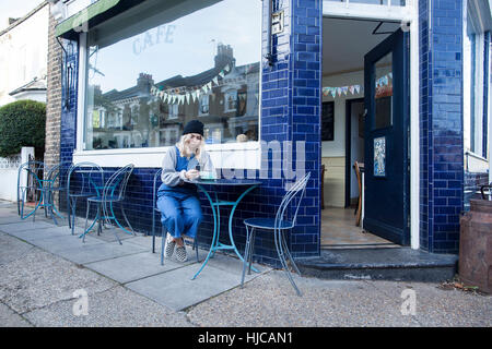 Jeune femme assise à l'extérieur à l'aide de café, téléphone intelligent Banque D'Images