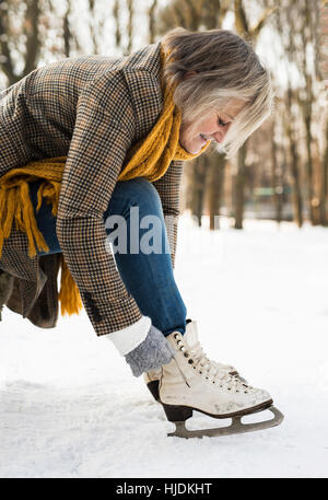 Senior woman in winter clothes mise sur de vieux patins à glace. Banque D'Images