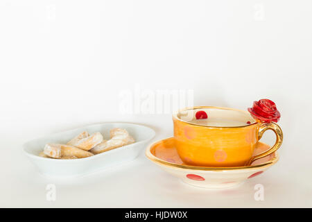 Un bel orange fait main golden cup avec ornement rose rouge, de lait et de délicieux biscuits sur une plaque blanche Banque D'Images