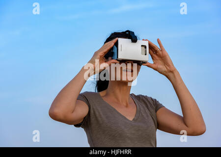 Femme (dans les années 40) le port d'un casque de réalité virtuelle (VR) masque le ciel avec quelques nuages derrière elle. Banque D'Images