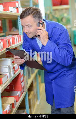 L'homme dans les magasins sur téléphone holding clipboard Banque D'Images